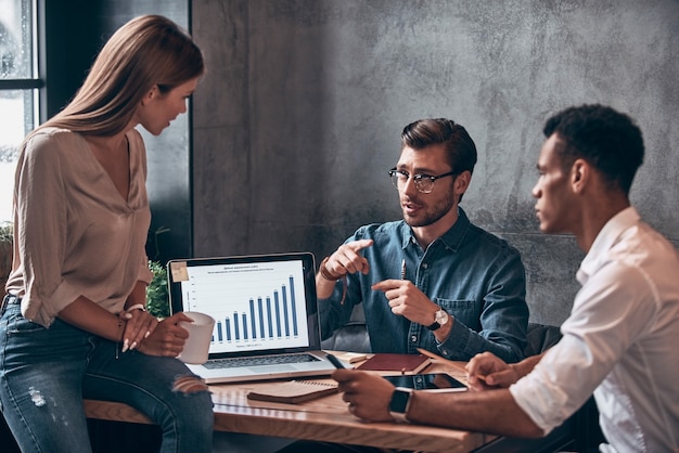 Group of young people in smart casual wear analyzing data on laptop while working in the office