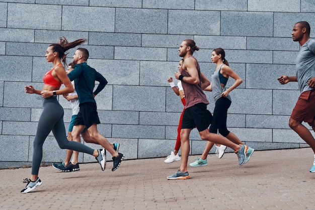 Gruppo di giovani in abbigliamento sportivo che fanno jogging mentre si esercitano sul marciapiede all'aperto