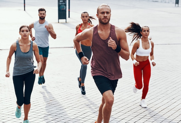 Group of young people in sports clothing jogging while exercising on the sidewalk outdoors