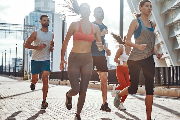 Group of young people in sports clothing jogging while exercising on the sidewalk outdoors