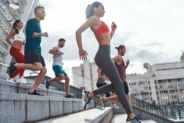 Group of young people in sports clothing jogging while exercising on the stairs outdoors