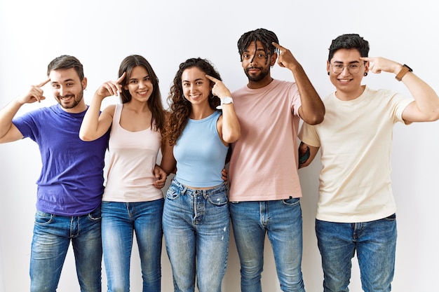 Group of young people standing together over isolated background smiling pointing to head with one finger great idea or thought good memory