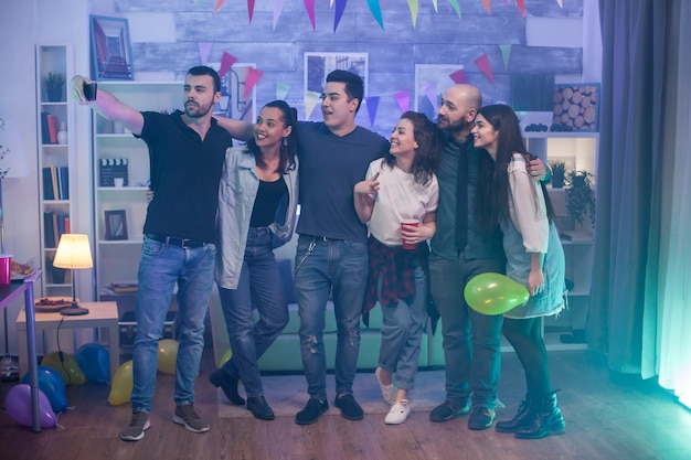 Photo group of young people taking a selfie at a party in an apartment