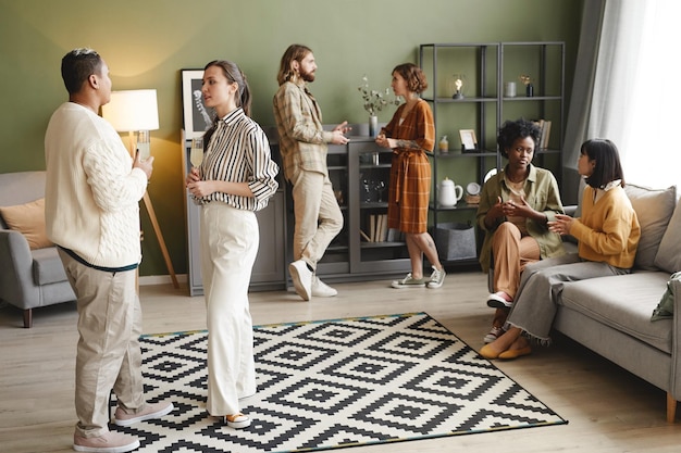 Group of young people talking to each other and drinking wine during home party in the living room