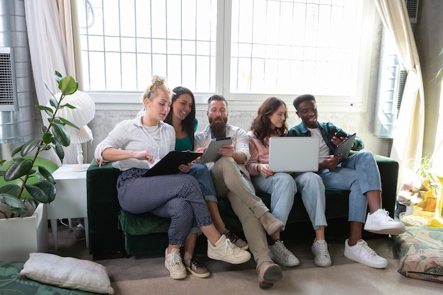 group of young people using digital devices on sofa at home