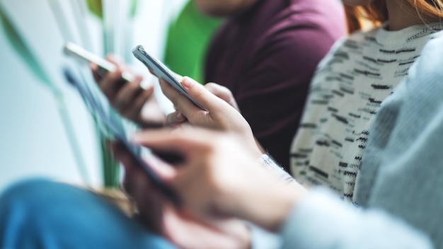 Photo group of young people using and looking at mobile phone while sitting together