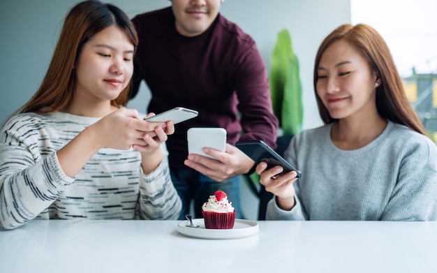 カフェで食べる前に携帯電話を使用してカップケーキの写真を撮る若者のグループ