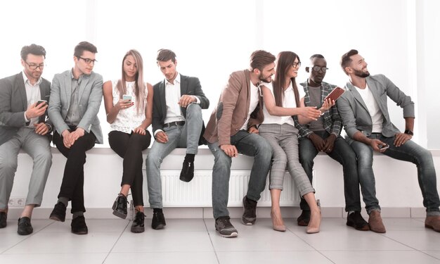 Photo group of young people using their gadgets sitting in the lobby of the office