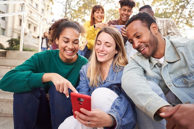group of young people watching something at and using phone sitting on stairs students lifestyle