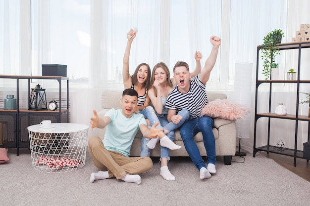 Group of young people watching tv. Active youth at home cheering on the team. Cheerful friends indoors having fun together.