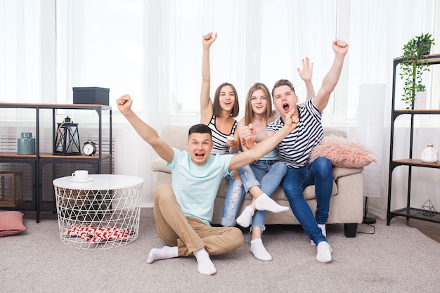 Group of young people watching tv. Active youth at home cheering on the team. Cheerful friends indoors having fun together.