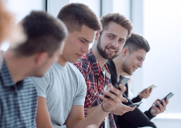 Group of young people with smartphones sitting in one row