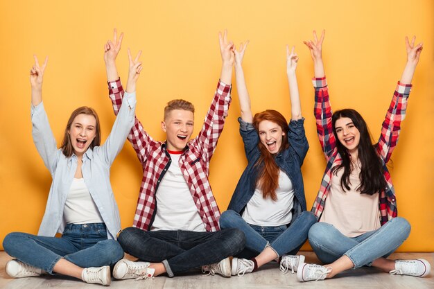 Group of young positive school friends sitting with hands raised