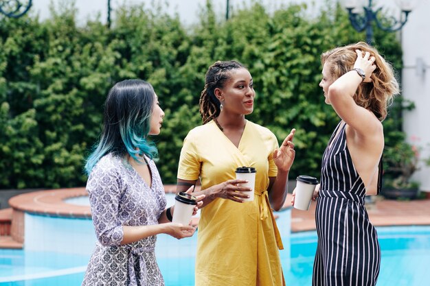 Group of young pretty multi-ethnic businesswomen drinking coffee and discussing news during coffee break