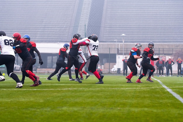 Group of young professional american football players in action\
during training match on the stadium field