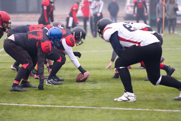 Group of young professional american football players ready to\
start during training match on the stadium field