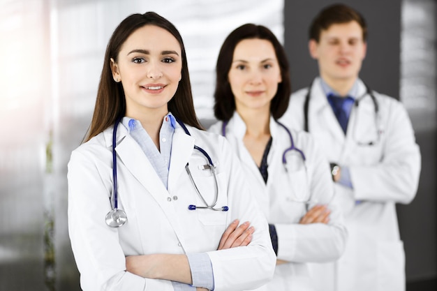 Group of young professional doctors standing as a team with arms crossed in sunny hospital. Medical help, insurance in health care, best disease treatment and medicine concept.