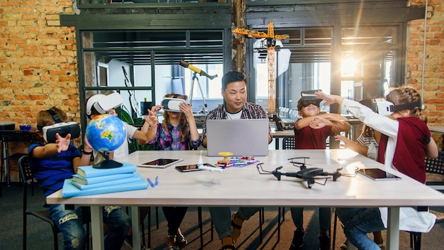 Group of young pupils of elementary school using virtual reality glasses during computer coding class.