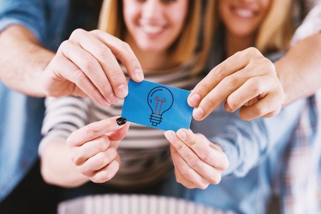 Group of young smiling designers holding together a blue note sticker .