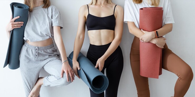 Photo 白い壁に立っているヨガマットを持つ若いスポーツの女の子のグループフィットネスや屋内でのヨガの後にリラックスするジムのガールフレンド