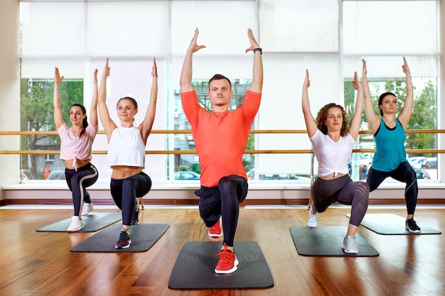 Group of young sporty attractive people practicing yoga lesson with instructor standing together in exercise working out full length studio background close up