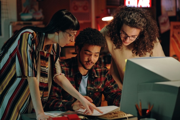 Photo group of young startups discussing blueprint together at table in front of computer