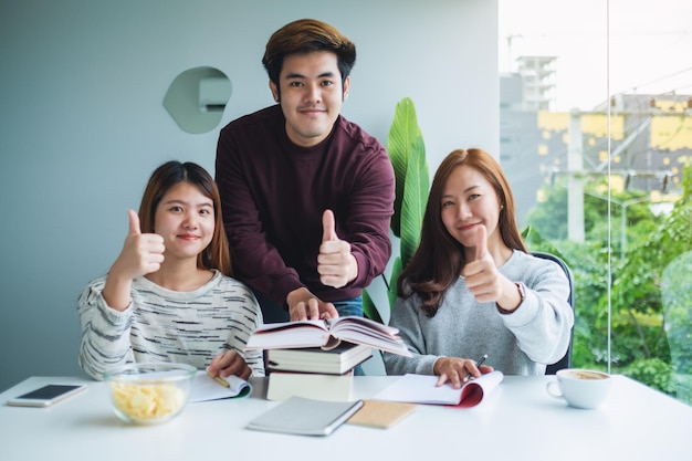 A group of young student making thumb up hands sign while tutoring and catching up workbook together