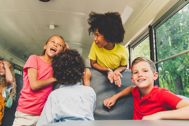 Gruppo di giovani studenti che frequentano la scuola primaria su uno scuolabus giallo - bambini delle scuole elementari che si divertono