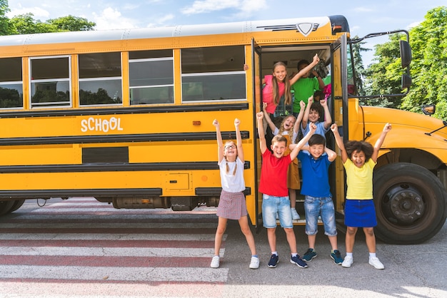 Группа молодых учеников начальной школы на желтом школьном автобусе - дети начальной школы веселятся