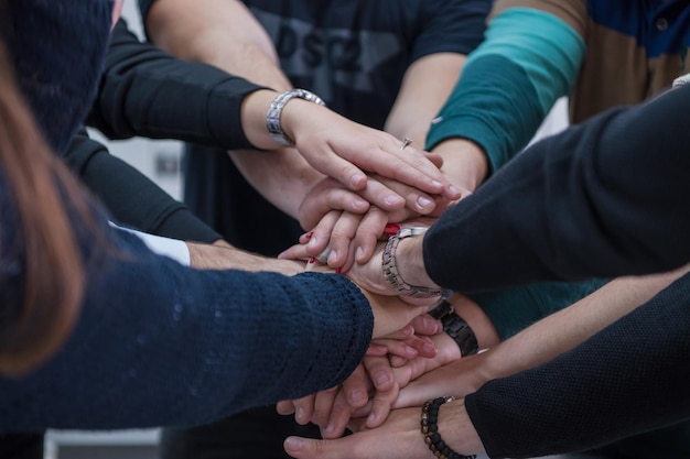 Group of young students in electronics classroom celebrating successfully finished project with holding their hands together, education and technology concept