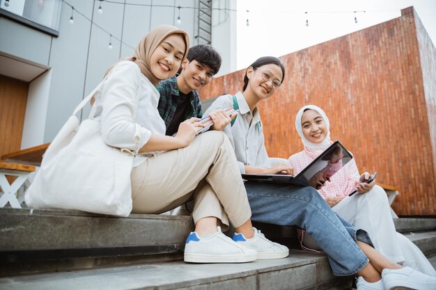 Group of young students smiling at the camera using a laptop sitting on the steps in a cafe