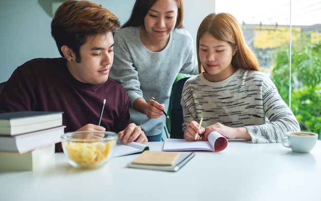 Group of young students tutoring and  catching up workbook with friends