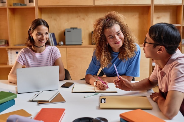 Gruppo di giovani studenti che lavorano insieme a un progetto seduti a tavola nella lounge della biblioteca