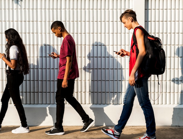 Group of young teenager friends walking home after school using smartphones