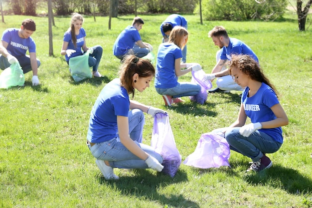 Photo group of young volunteers gathering garbage in park