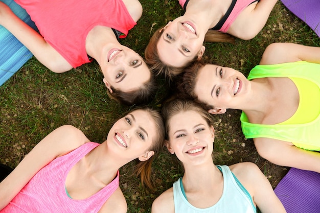 Group of young women lying on lawn after practicing yoga outdoors