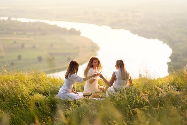 Photo group of young women sitting on grass on summer evening