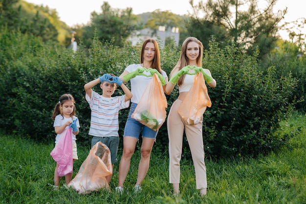 Un gruppo di giovani donne con bambini mostra i cuori dopo aver pulito la spazzatura nel parco durante il tramonto. cura dell'ambiente, riciclaggio.