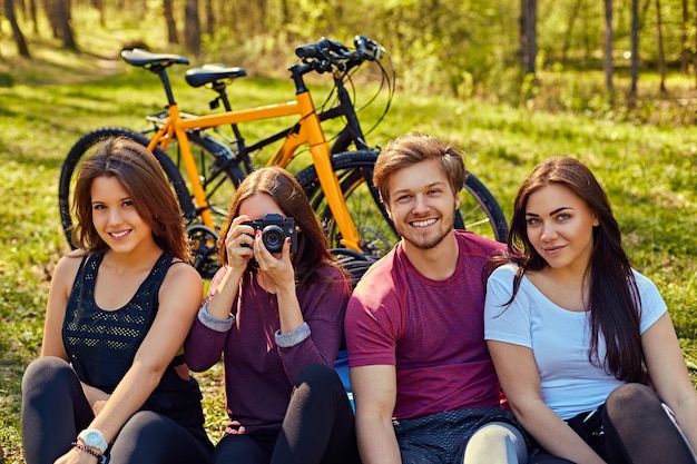 森で自転車に乗った後にリラックスする人々のグループ。デジタルコンパクトフォトカメラで写真を撮る女性。
