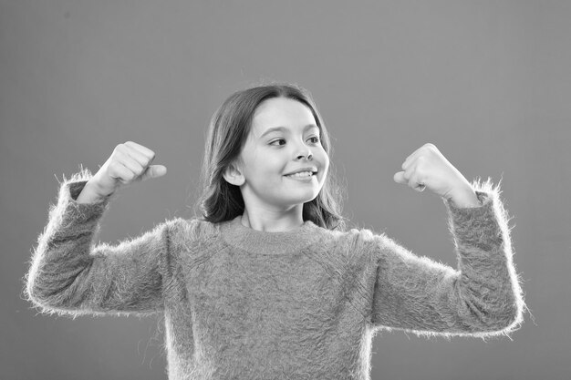 Grow up strong and confident feel power of herself cheerful child orange backdrop carefree childhood healthy and powerful happy childrens day cute little girl smiling small kid show biceps