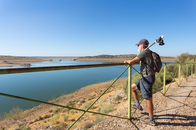 Grown man rests on fence and looks out over swamp