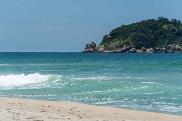 Grumari beach near Barra da Tijuca in Rio de Janeiro, Brazil. Sunny day with blue sky, clear water and small waves. Hills and nature around.