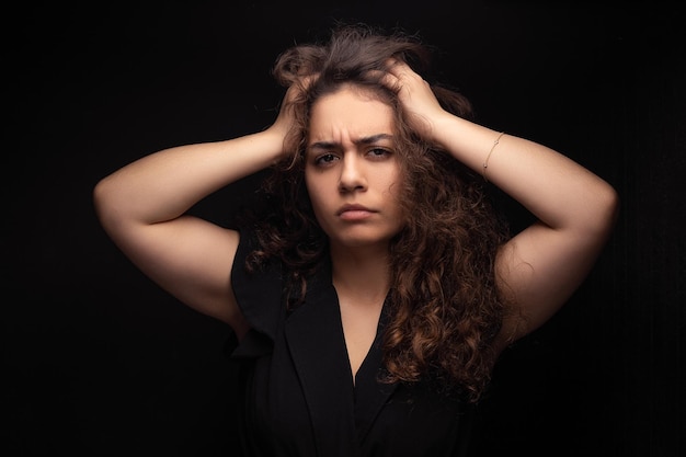 Grunge portrait of a depressed and sad woman with her hands touching her forehead isolated on a black background