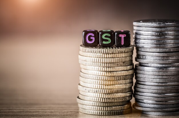 GST Concept with alphabet block on a gold stacked of coins. 