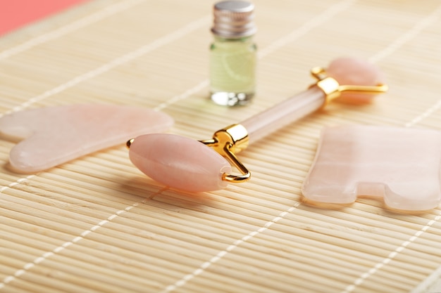 Gua sha massage made of natural rose Quartz-roller, jade stone and oil, on a bamboo background for face and body care.