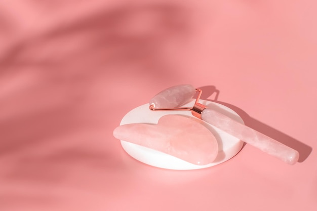 Gua Sha massage tools on pink background. Quartz roller, facial massage and relaxation. Anti age and lifting at home.