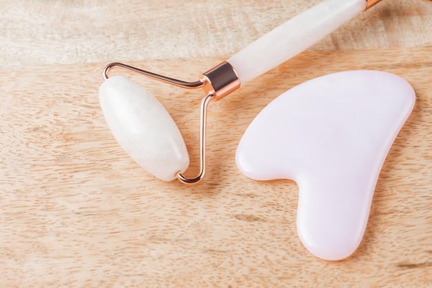 Gua Sha massager and rose quartz massage roller on wooden background Pink jade stone for face and body care Horizontal shoot Flat lay top view Copy space for your text