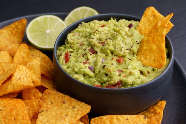 Salsa di guacamole con tortilla chips o nachos in banda nera su fondo nero