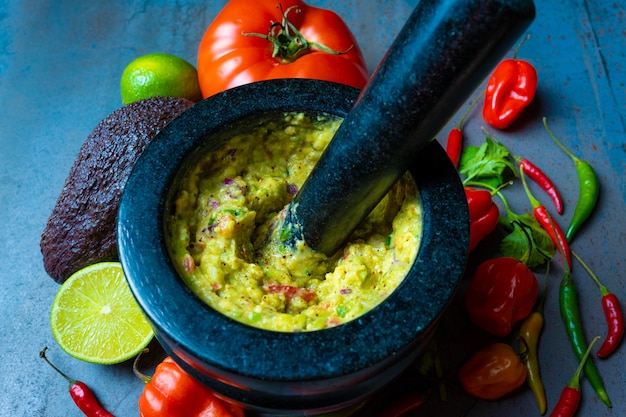 guacamole mexican food on mortar with vegetables and textured background