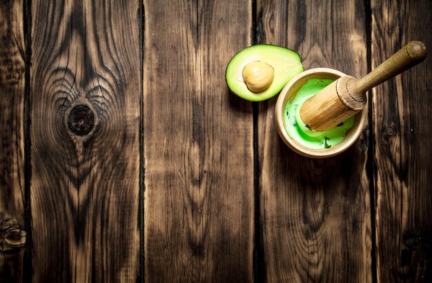 The guacamole in a mortar with pestle. On wooden background.